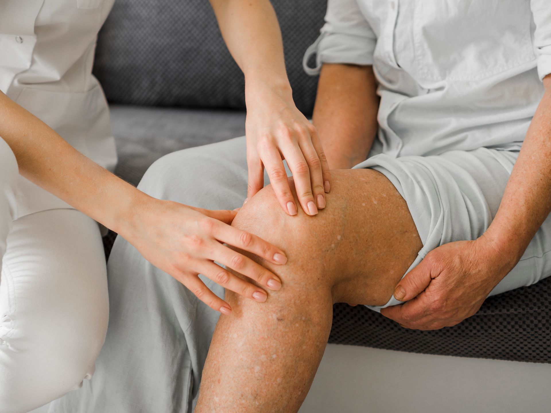 A nurse is examining a patient 's knee while the patient is sitting on a couch.