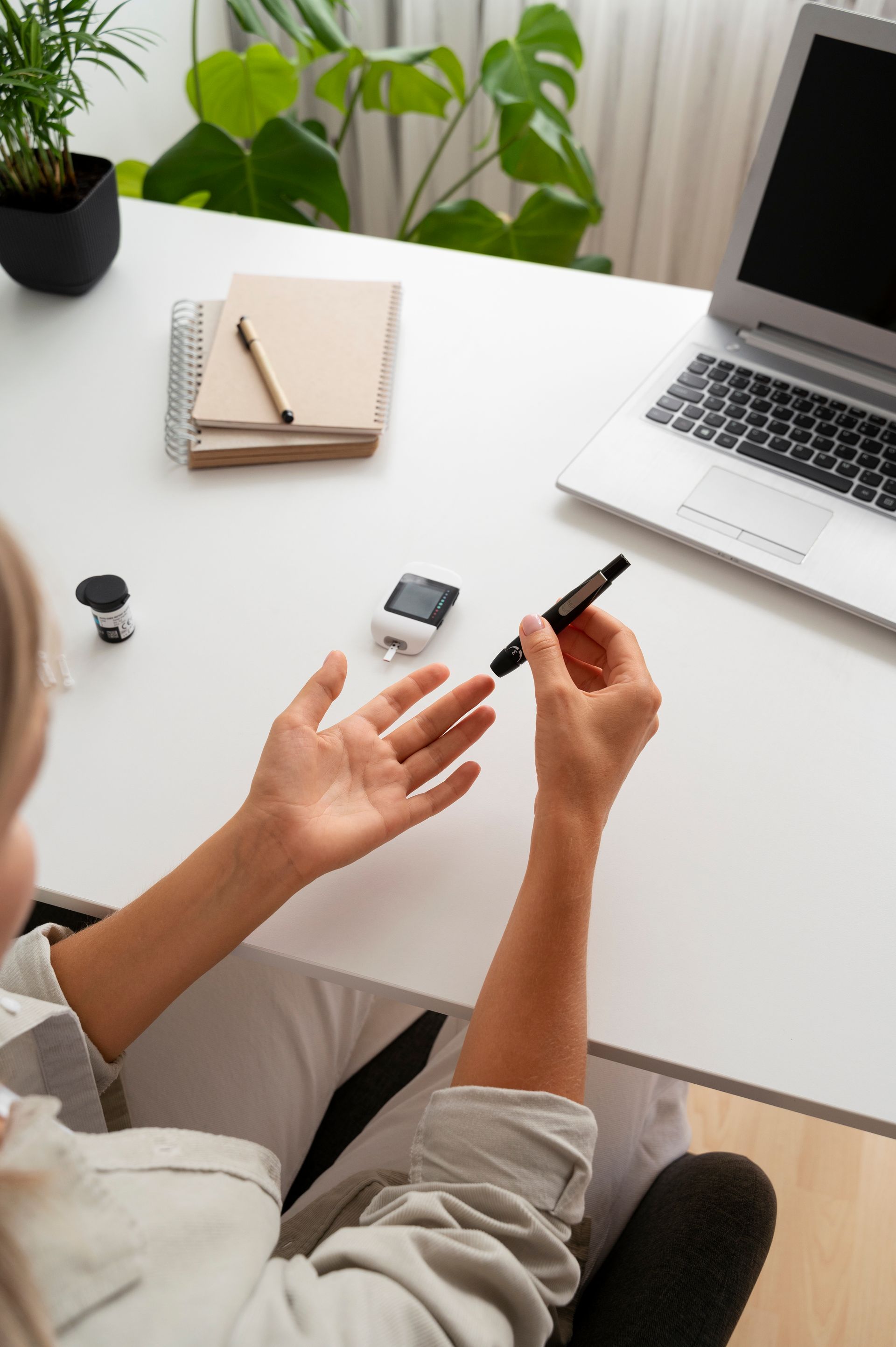 A woman is sitting at a desk with a laptop and a pen in her hand.