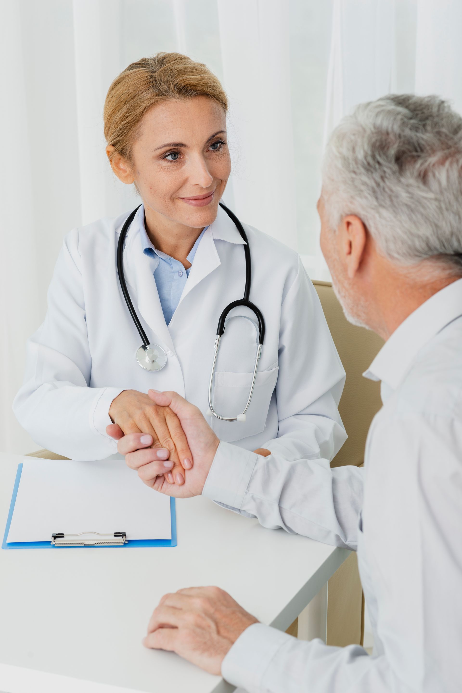 A doctor is shaking a patient 's hand while sitting at a desk.