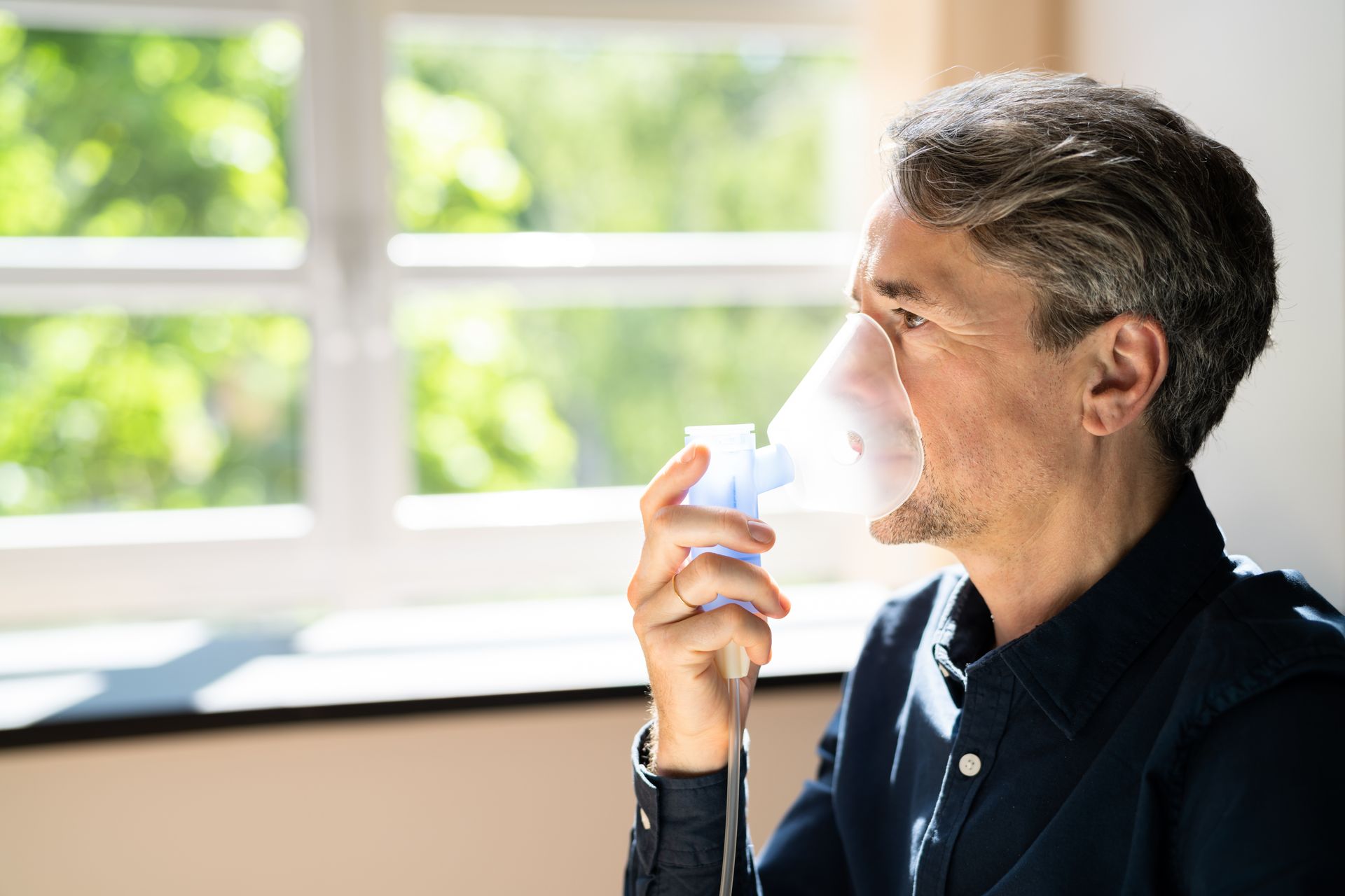 A man is using an oxygen mask in front of a window.