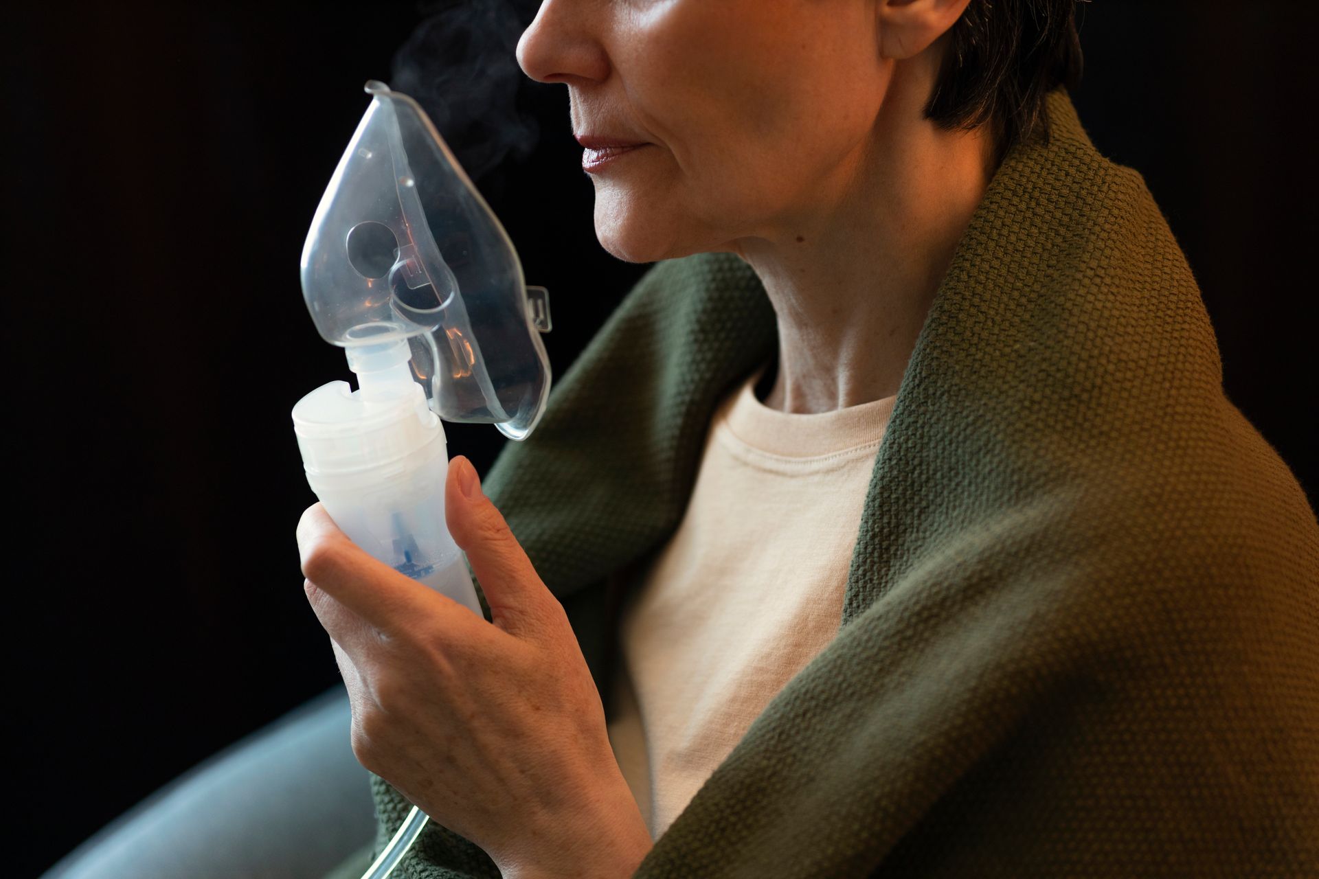 A woman wrapped in a blanket is using an oxygen mask.