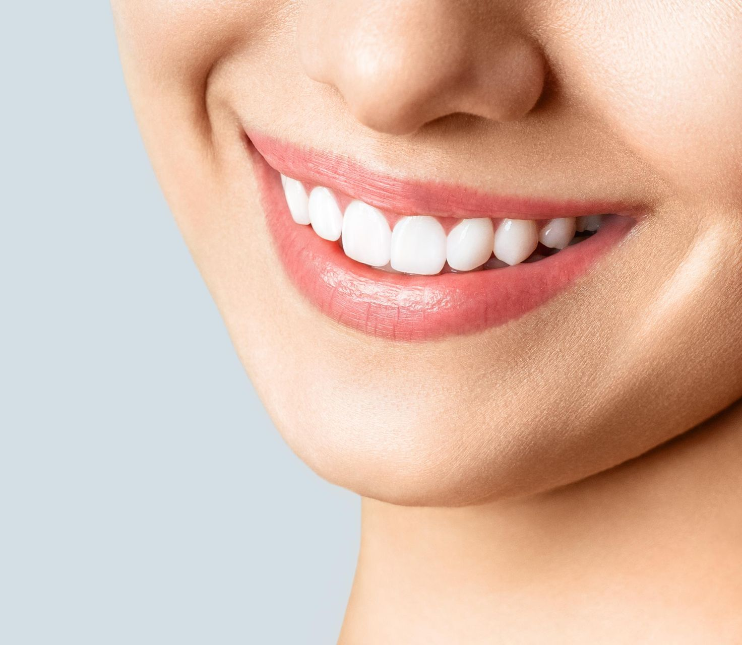 A close-up shot showing the lower half of a smiling face with bright, healthy white teeth against a light blue background.