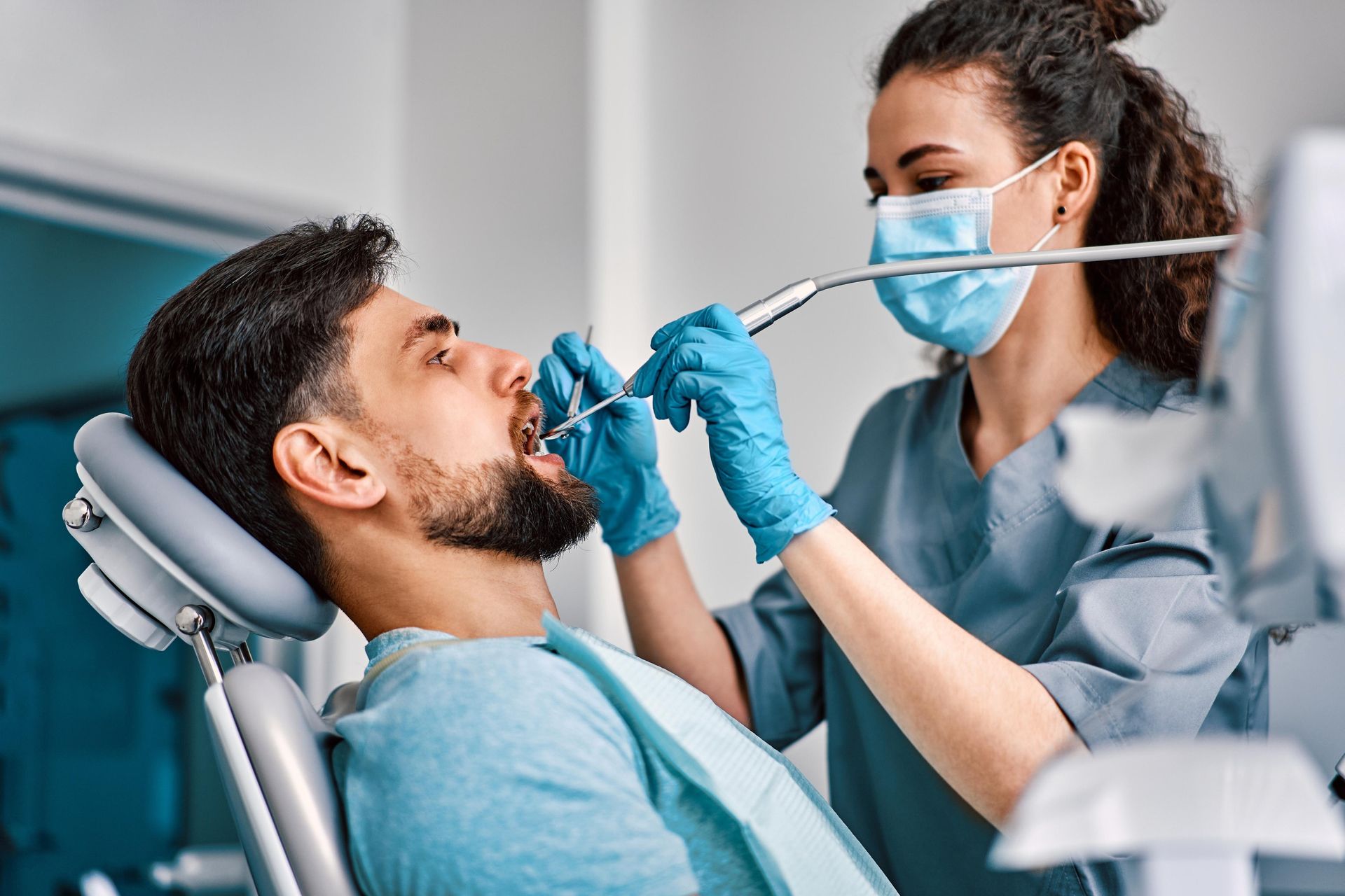 A dental professional in a mask and blue gloves examines a patient's teeth in a clinical setting.
