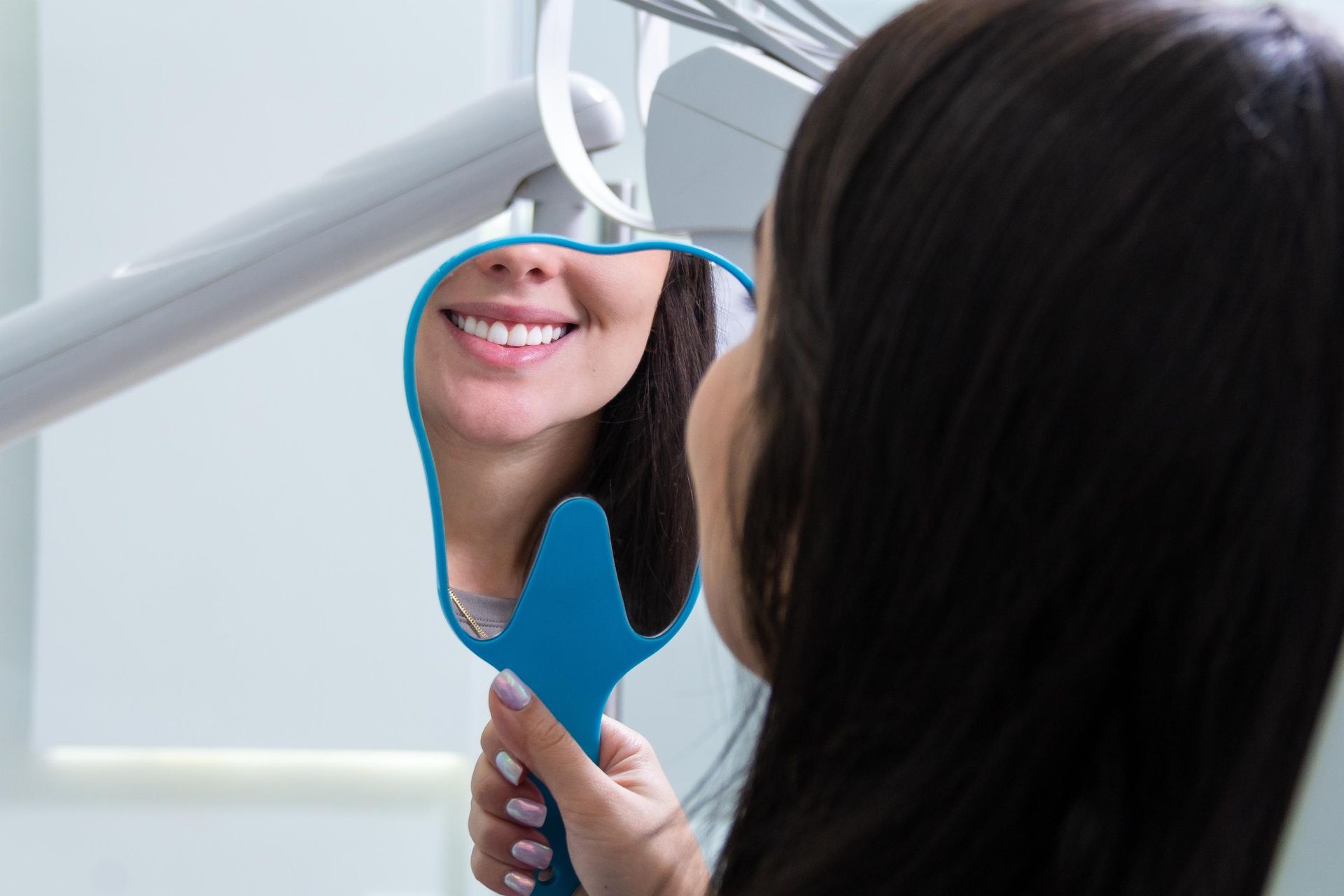 A person holds a tooth-shaped handheld mirror to view their smiling reflection in a dental office.