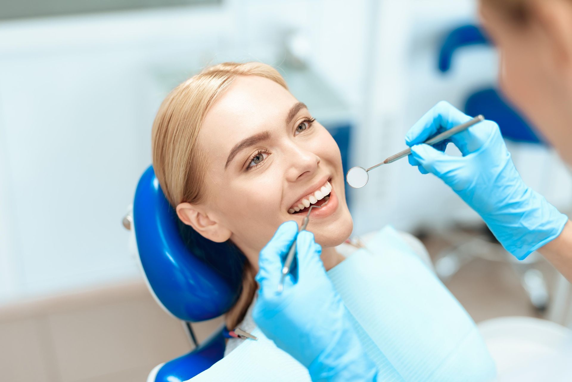 A smiling person in a dental chair receives a checkup from a dentist wearing blue nitrile gloves.
