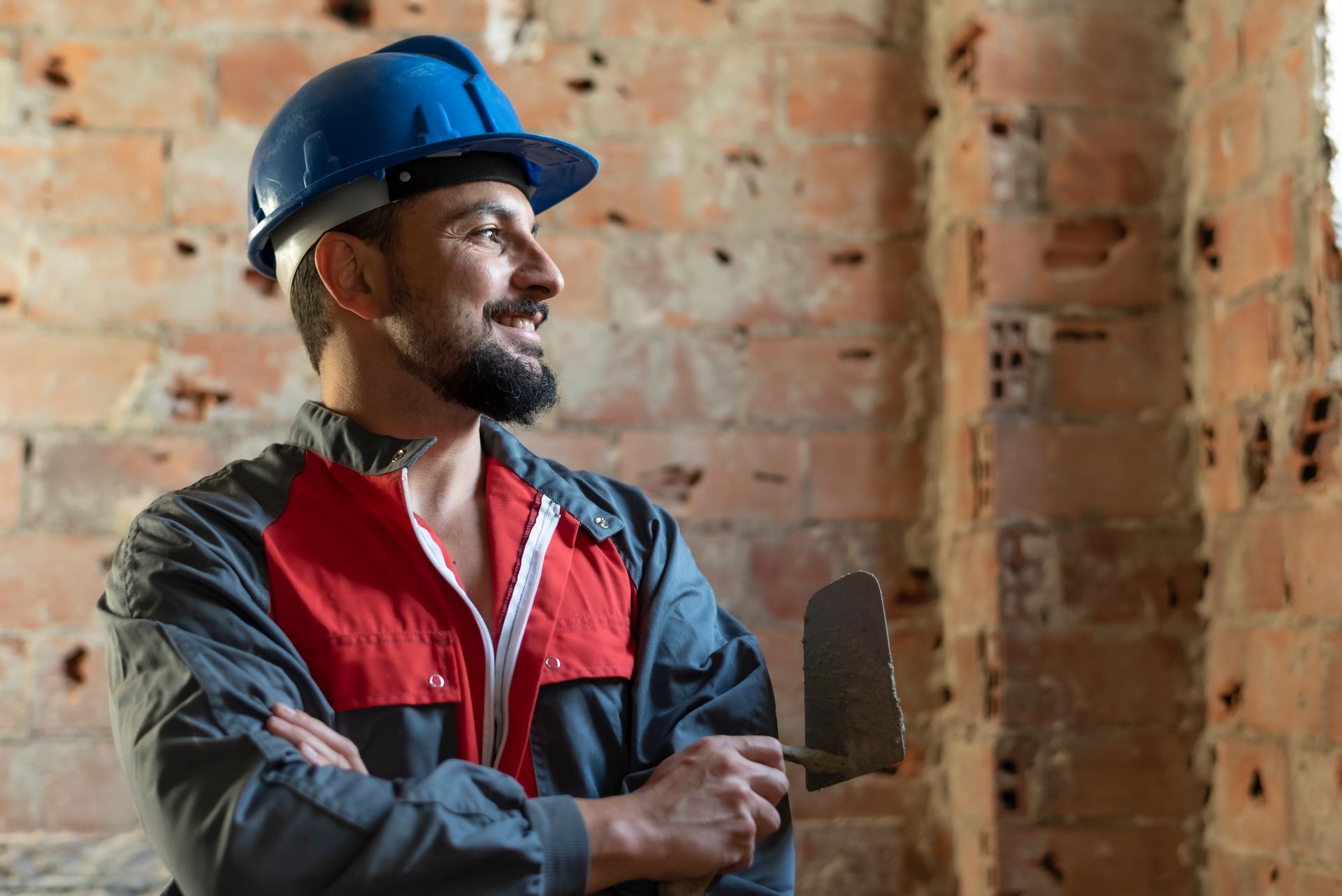A man wearing a hard hat and overalls is holding a trowel.