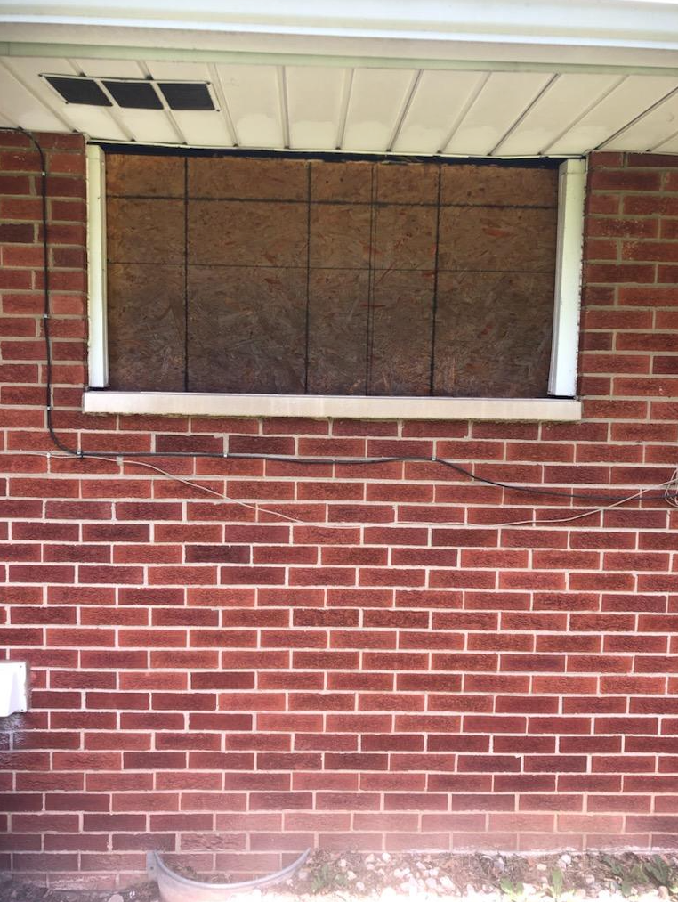 A brick wall with a window that has been boarded up