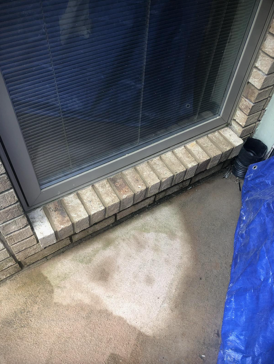 A brick wall with a sliding glass door and a blue tarp.