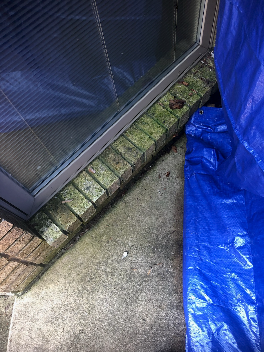 A blue tarp is sitting on the ground next to a brick wall.