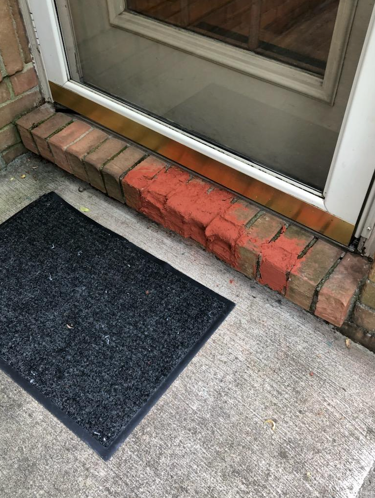 A black door mat is sitting under a brick door.
