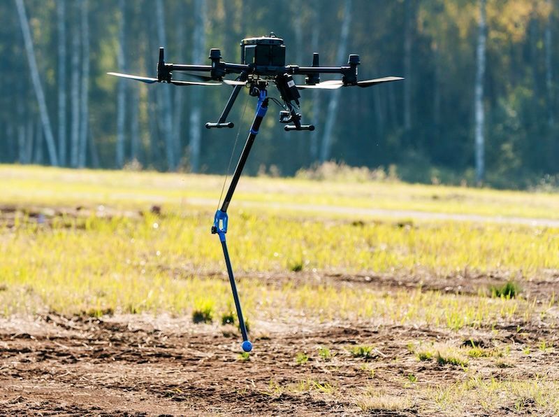 A drone is flying in the air with trees in the background.