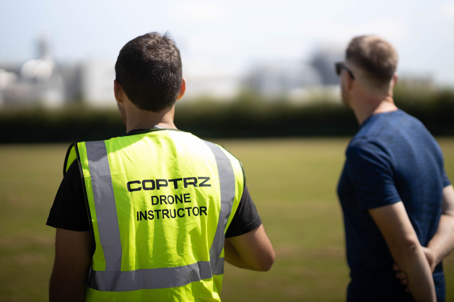 A man in a yellow vest is standing next to another man in a field.