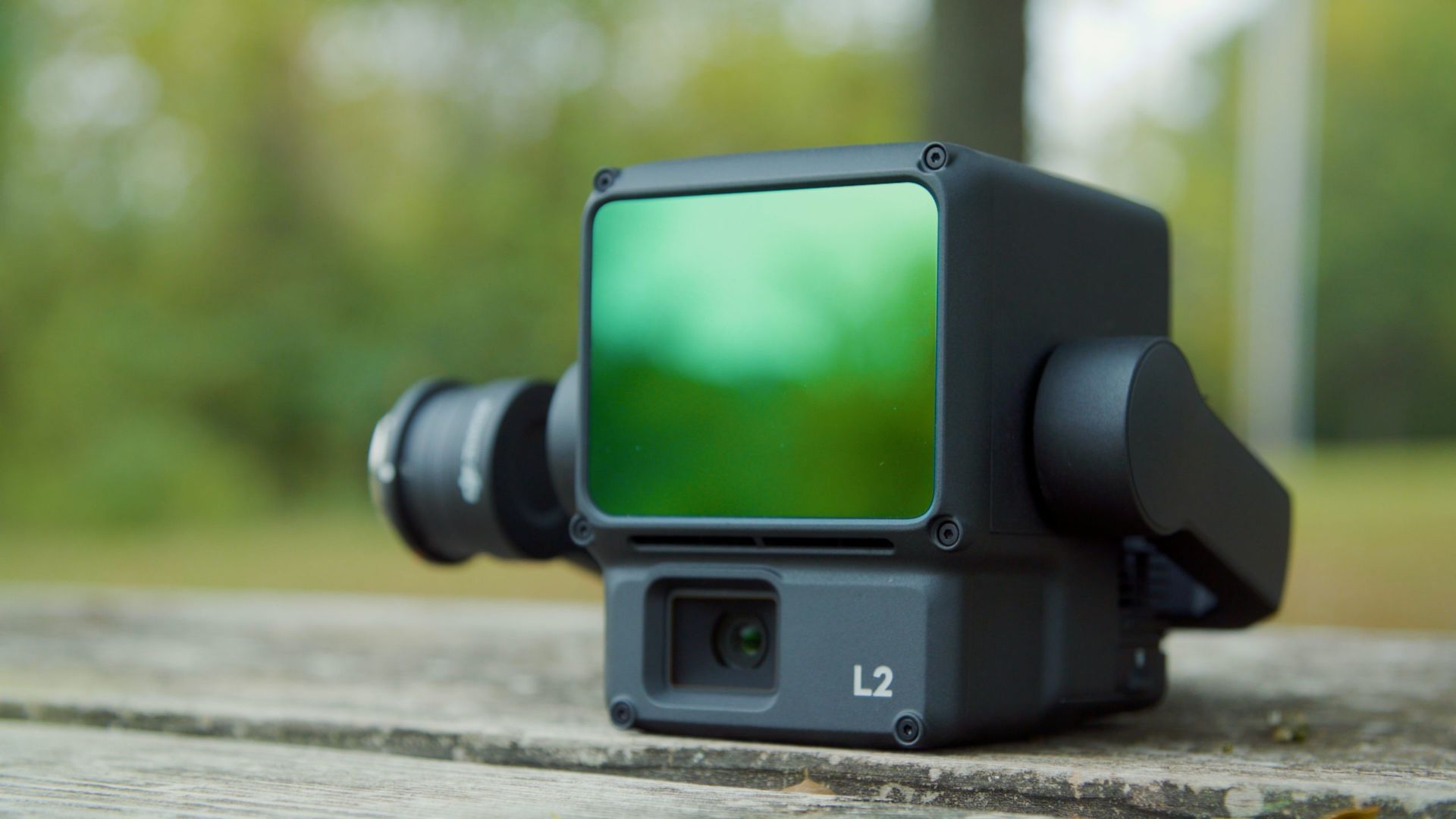 A camera with a green lens is sitting on a wooden table.