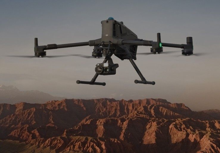 A drone is flying in the air with trees in the background.
