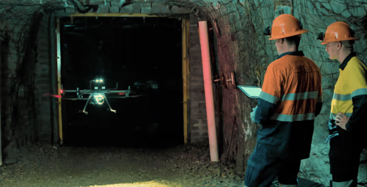 Zwei Männer mit Schutzhelmen beobachten eine Drohne, die durch einen dunklen Tunnel fliegt.