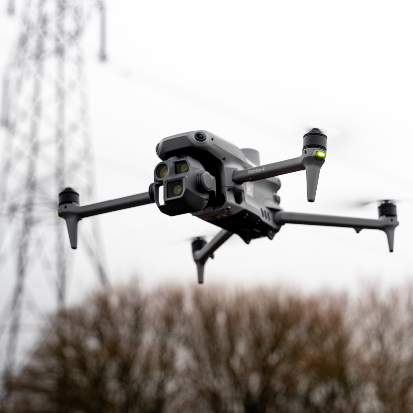 A drone is flying in the air with trees in the background.