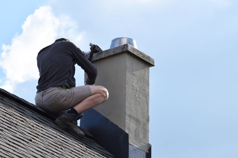 A Man is Kneeling on Top of a Roof Next to a Chimney — HTH Sheetmetal Mackay in Mackay, QLD