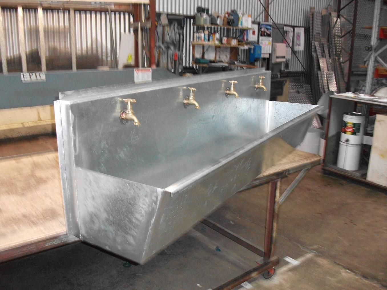 A Long Metal Sink With Gold Faucets is Sitting on a Wooden Table — HTH Sheetmetal Mackay in Mackay, QLD