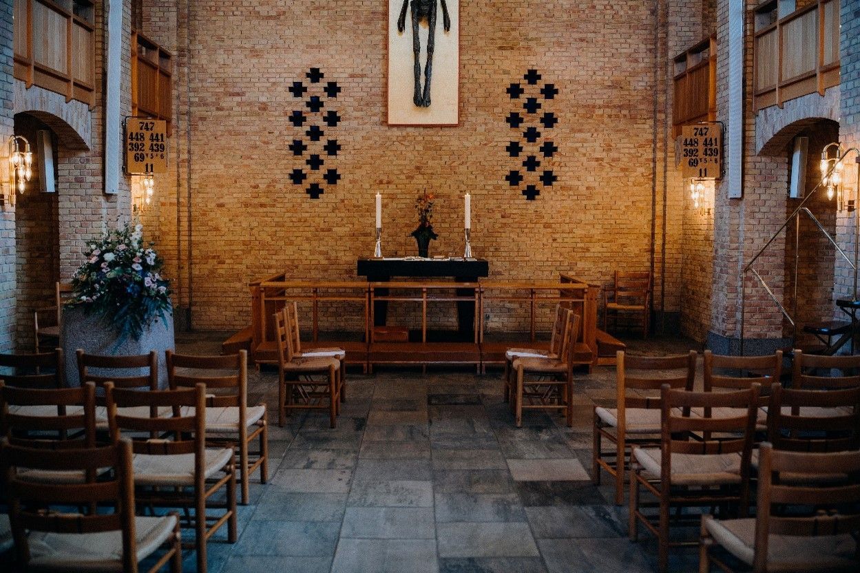 Small church interior with altar, wooden chairs, and stone floor, lit softly by daylight