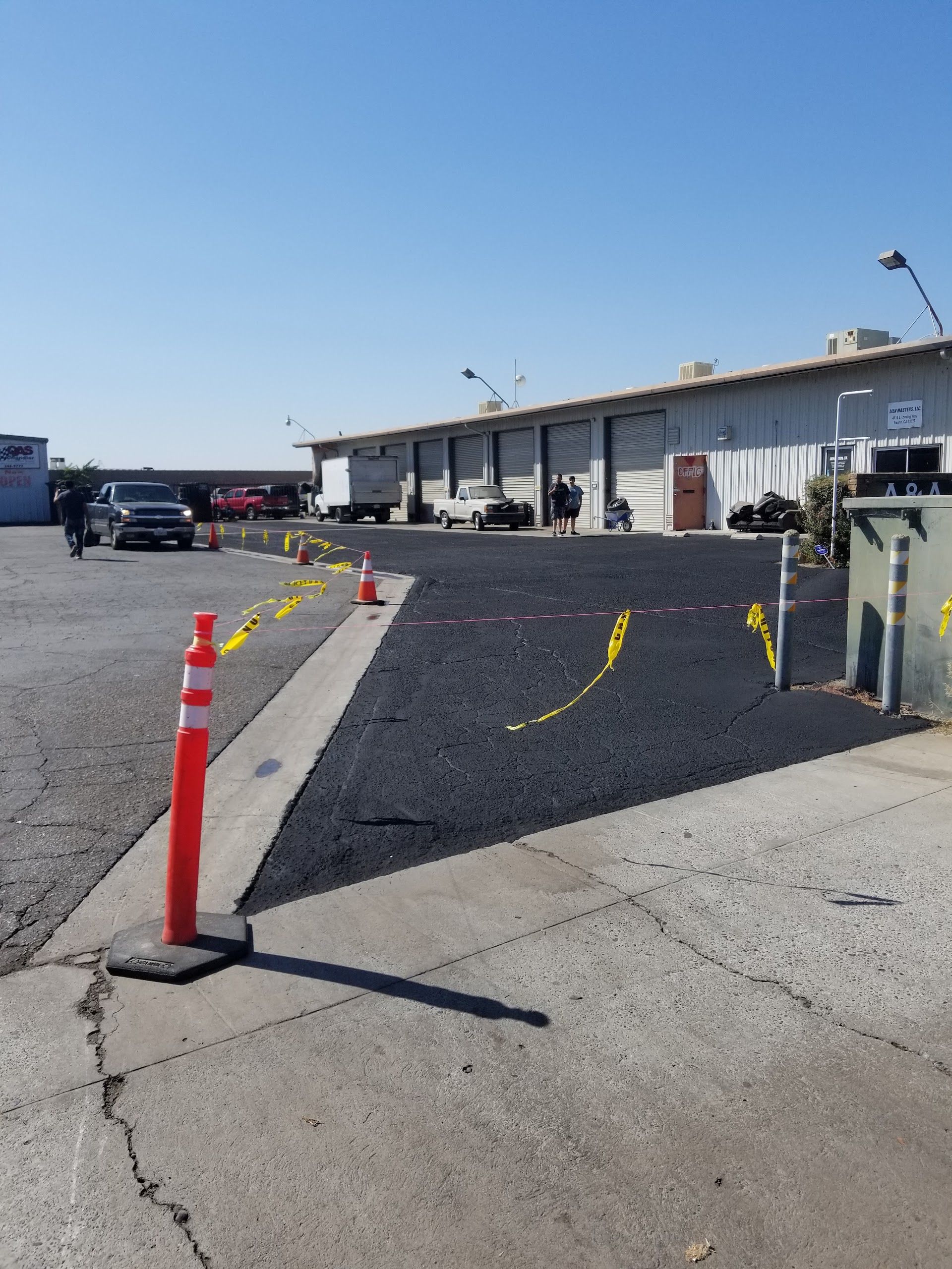New asphalt paving in front of warehouse; orange traffic cones and caution tape mark boundaries | My Automotive