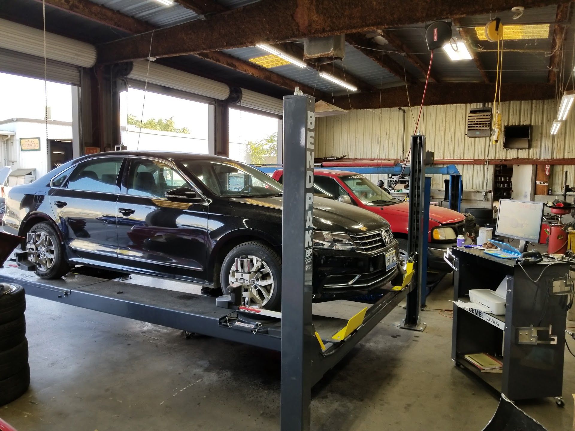 Black sedan on a car lift in a repair shop. Another car visible. Shop has tools and equipment | My Automotive