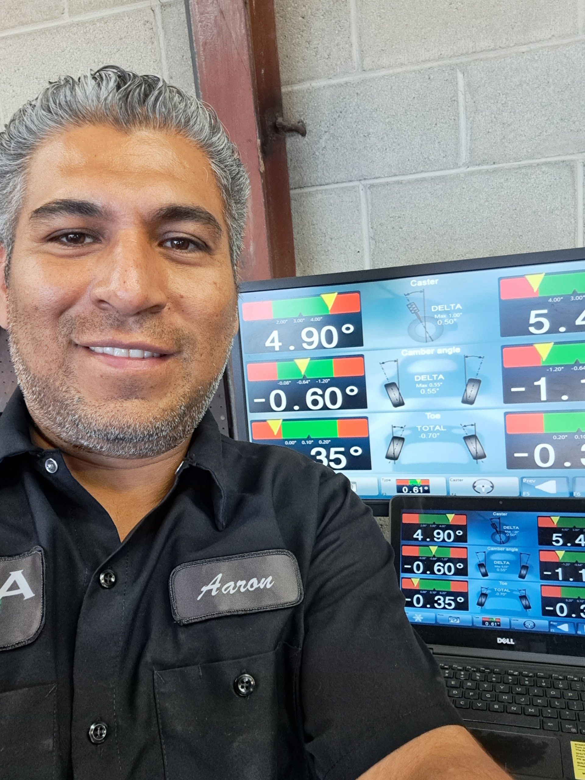 Mechanic smiling, in a shop, in front of alignment machine displays. Shows angle readings | My Automotive