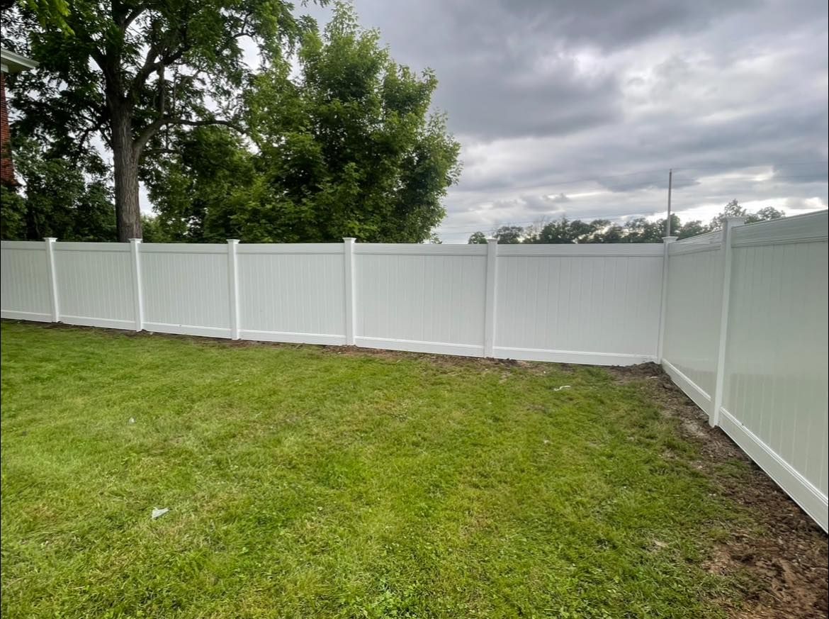 A white vinyl fence surrounds a lush green yard.