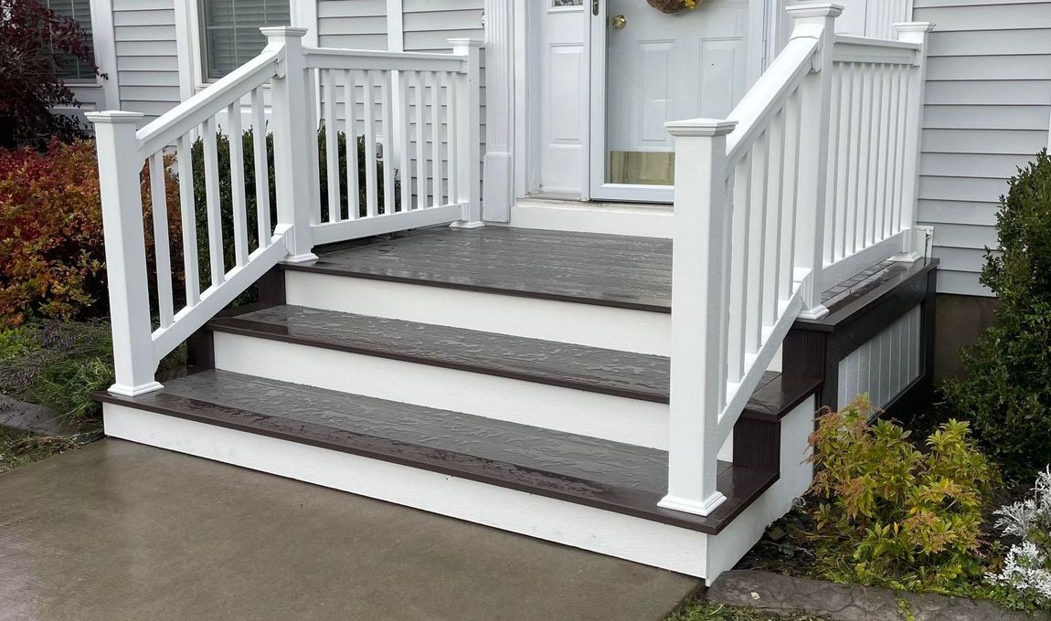 A white house with a porch and stairs in front of it.