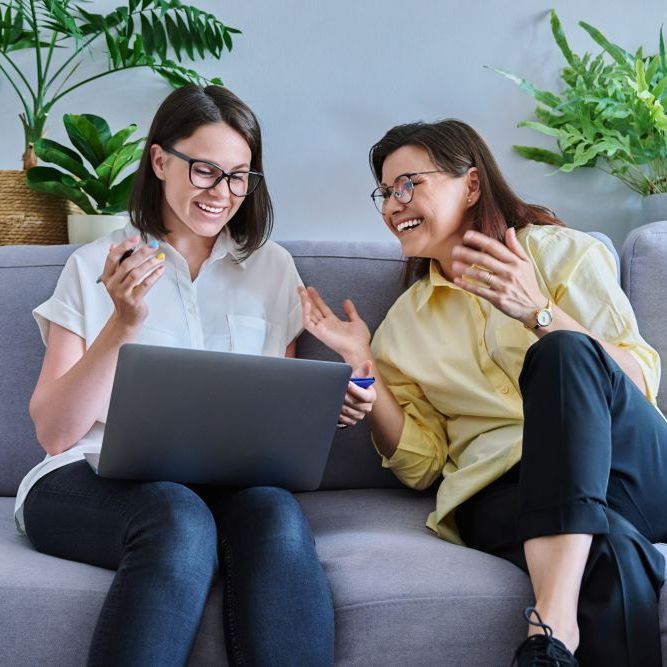 Two women are sitting on a couch looking at a laptop.