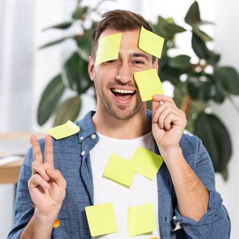 A man with sticky notes on his face is giving a peace sign.