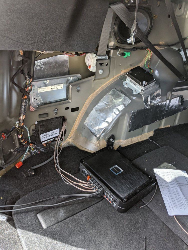 Car interior with amplifier and wiring installed, likely for audio upgrades.