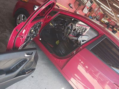 Red car in auto shop with open doors and exposed interior components.
