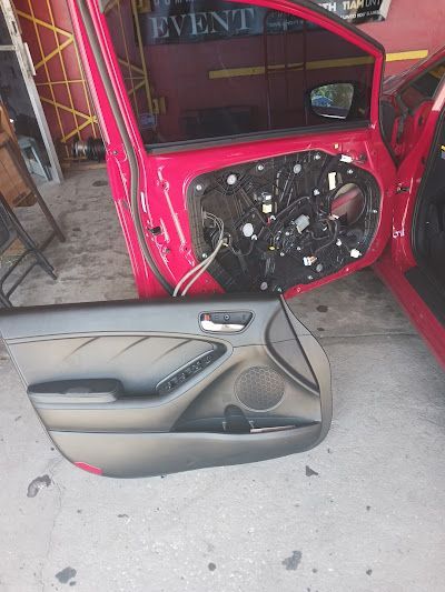Red car door with interior panel removed, exposing wiring. The panel lies on the floor.
