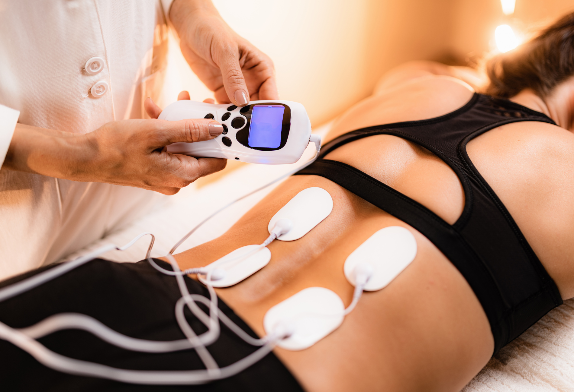 A woman is getting a massage with electrodes on her back.