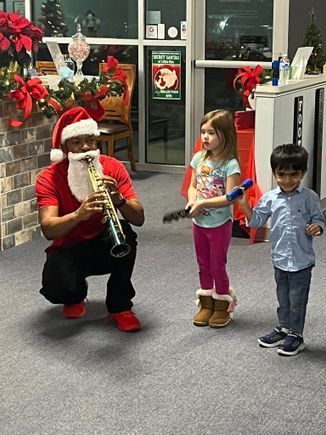A man dressed as santa claus is playing a trumpet for two children.