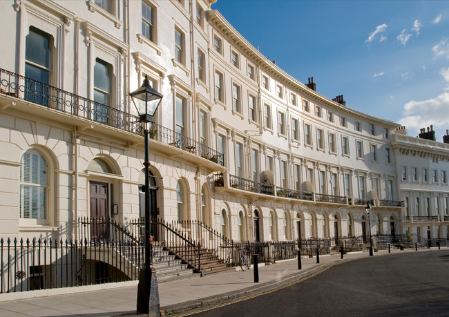 A curved row of elegant, cream-colored Victorian terraced houses with iron balconies under a clear blue sky.