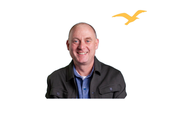A smiling person wearing a blue shirt under a dark jacket, with a small yellow seagull icon floating to their top right.