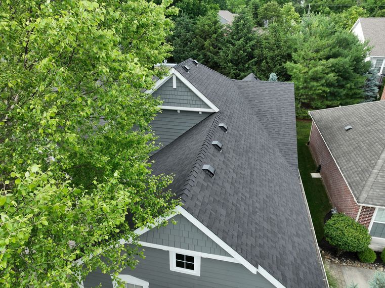 An aerial view of a house with a black roof surrounded by trees.