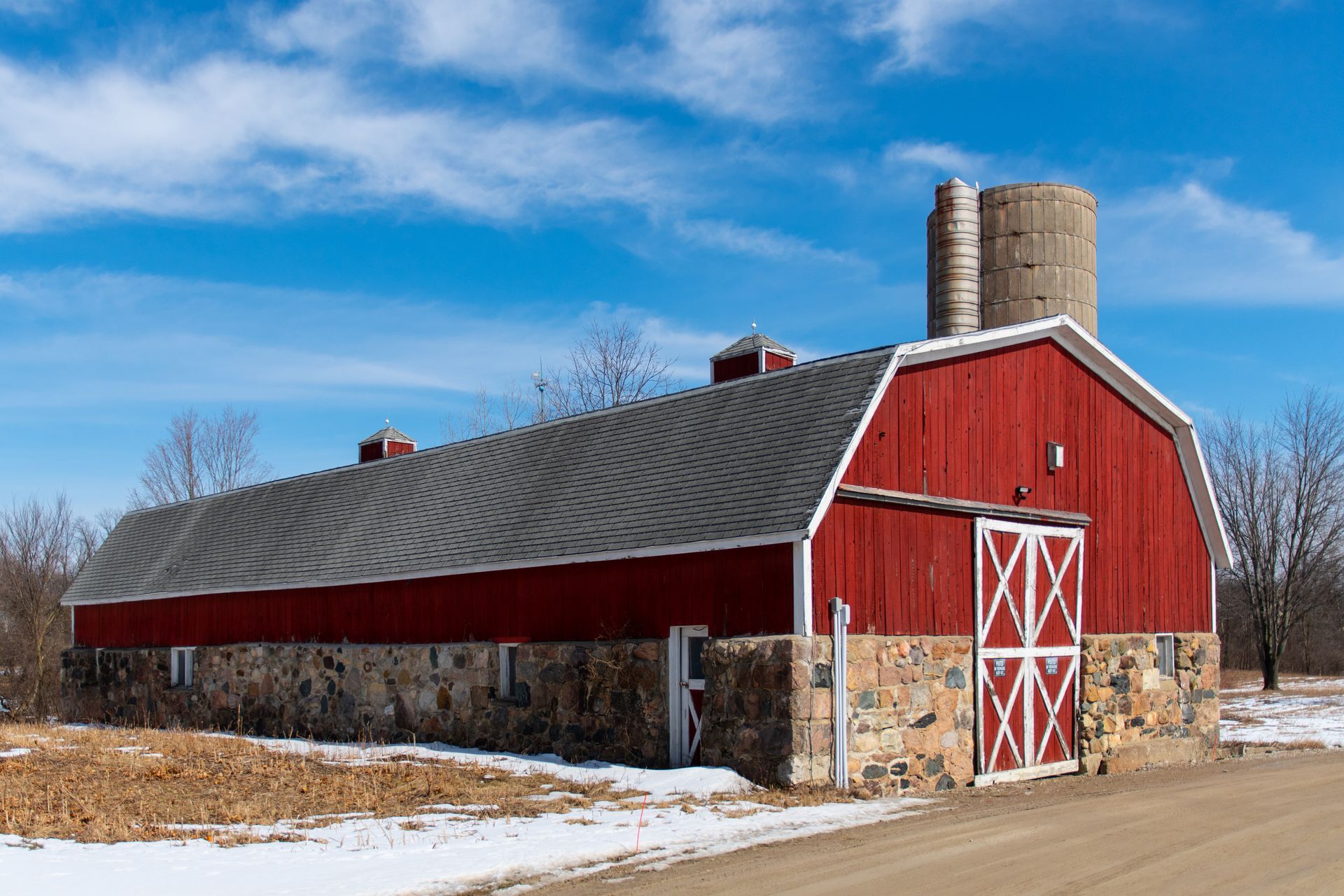 A red barn is sitting on the side of a dirt road.