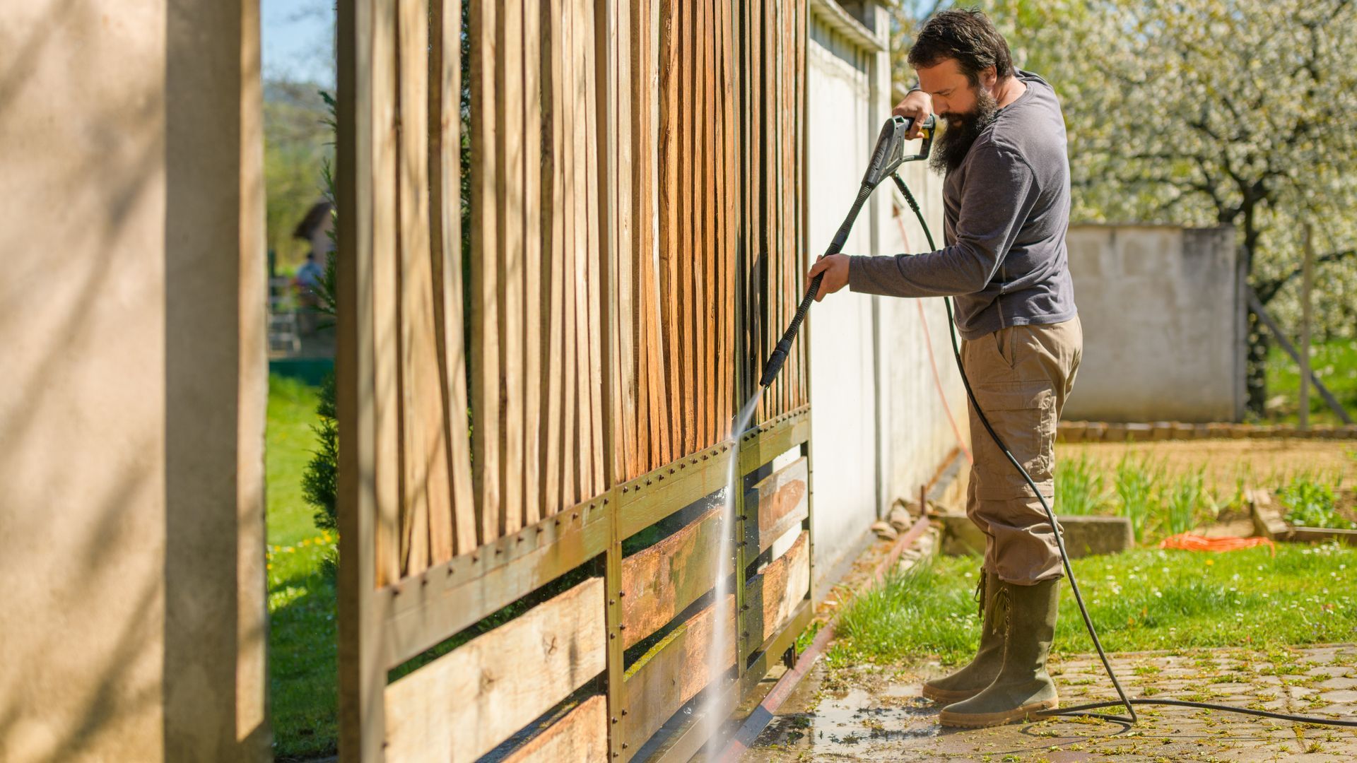 A man is cleaning a wooden fence with a high pressure washer.
