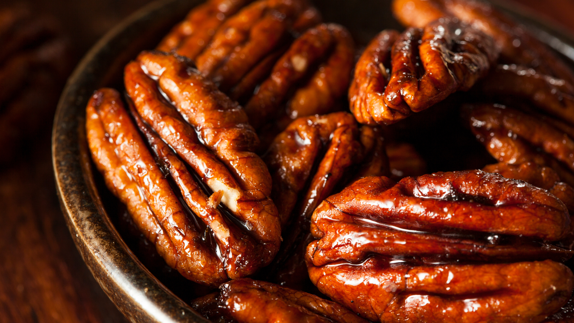 A close up of a bowl of pecans on a wooden table.