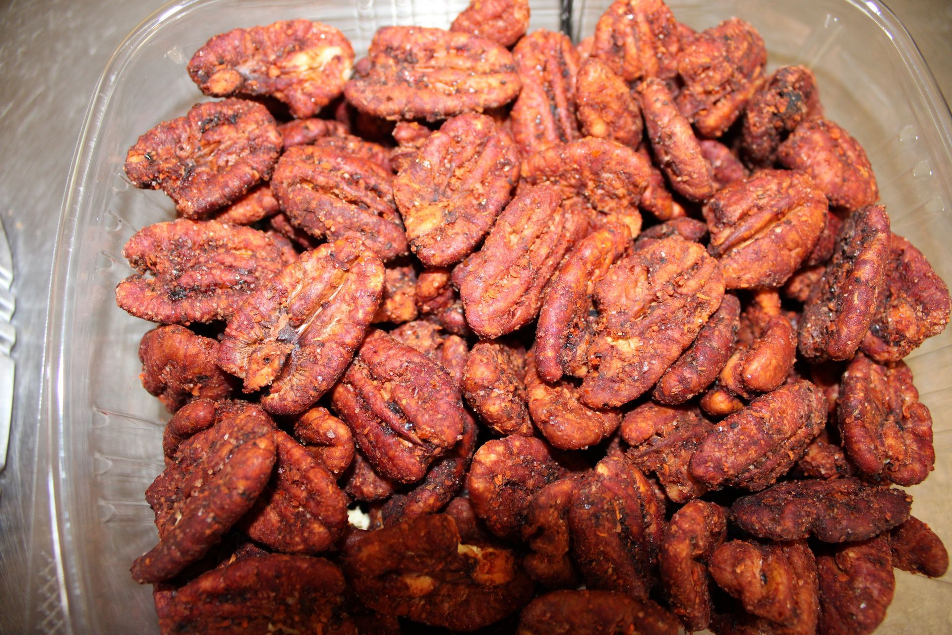A plastic container filled with roasted pecans is sitting on a table.