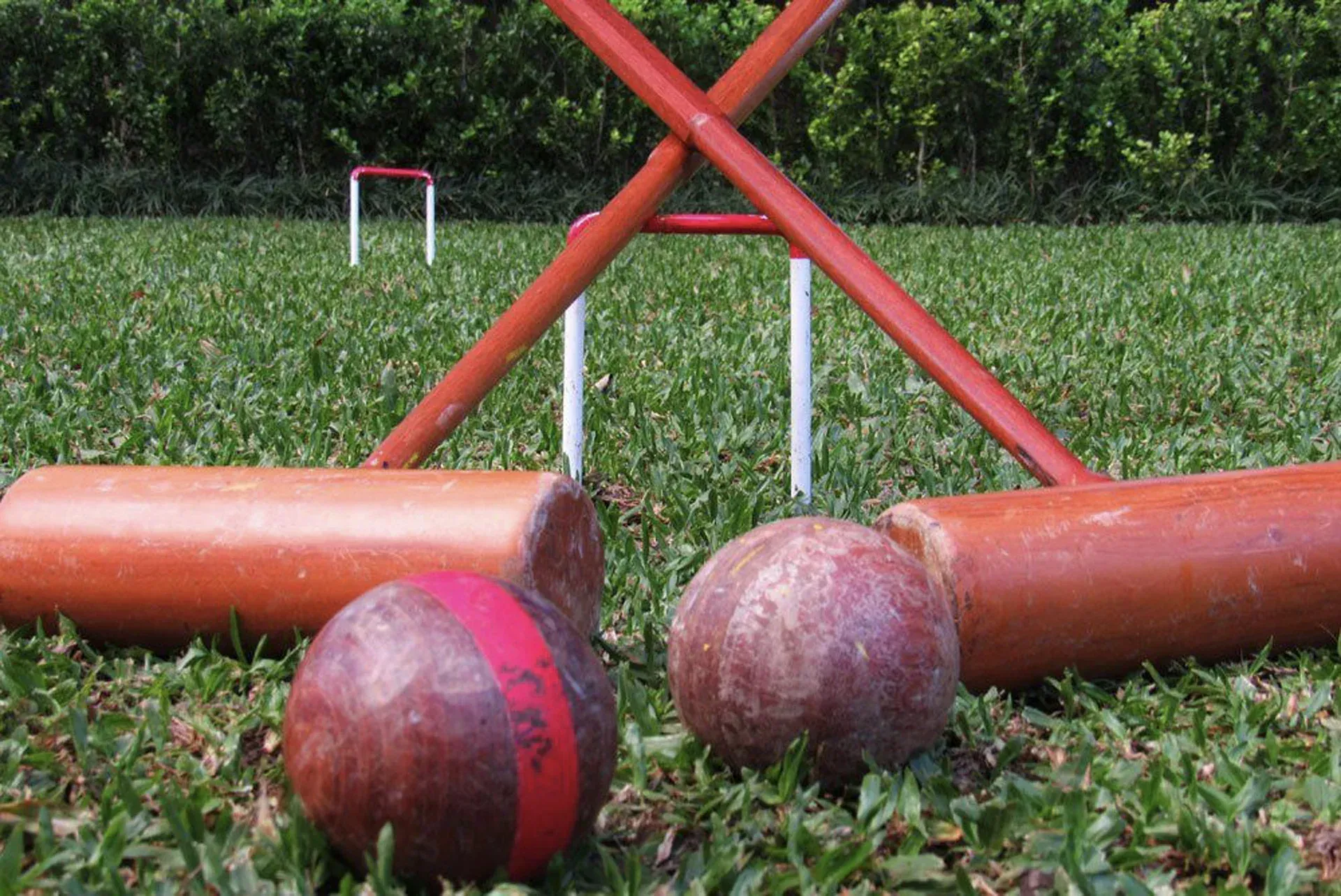 Gangorra vermelha de parque infantil com grandes bolas de madeira na grama ao ar livre, uma bola centralizada na frente.
