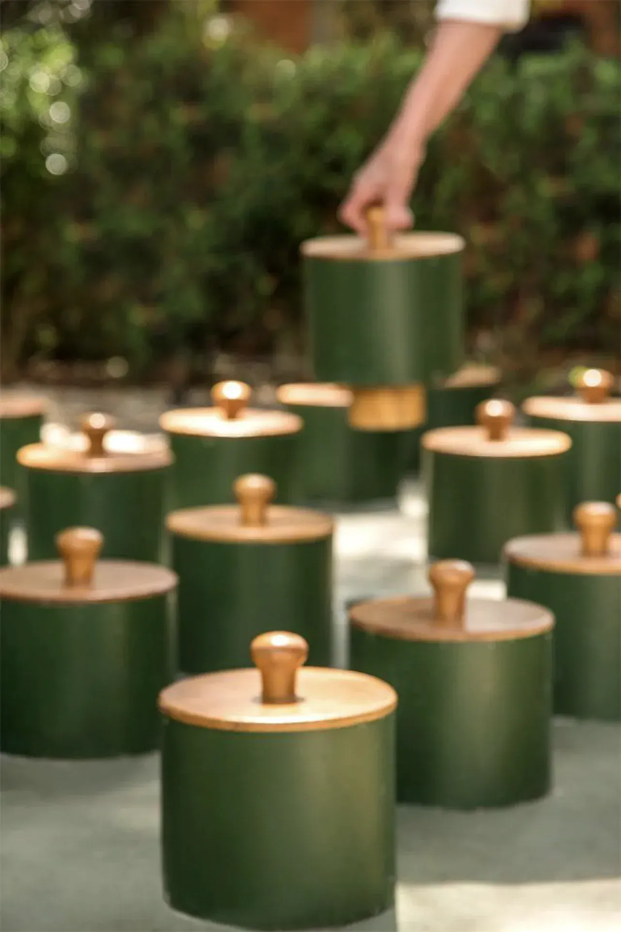 Velas verdes com tampas douradas dispostas sobre uma mesa, uma delas acesa manualmente.