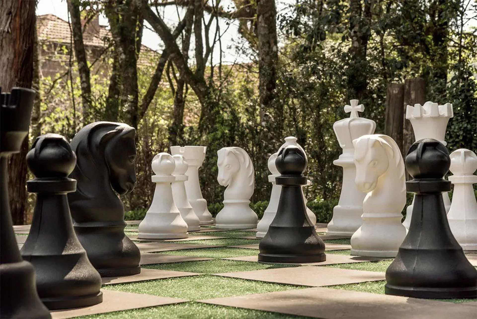 Peças gigantes de xadrez em preto e branco num tabuleiro ao ar livre num parque ensolarado.