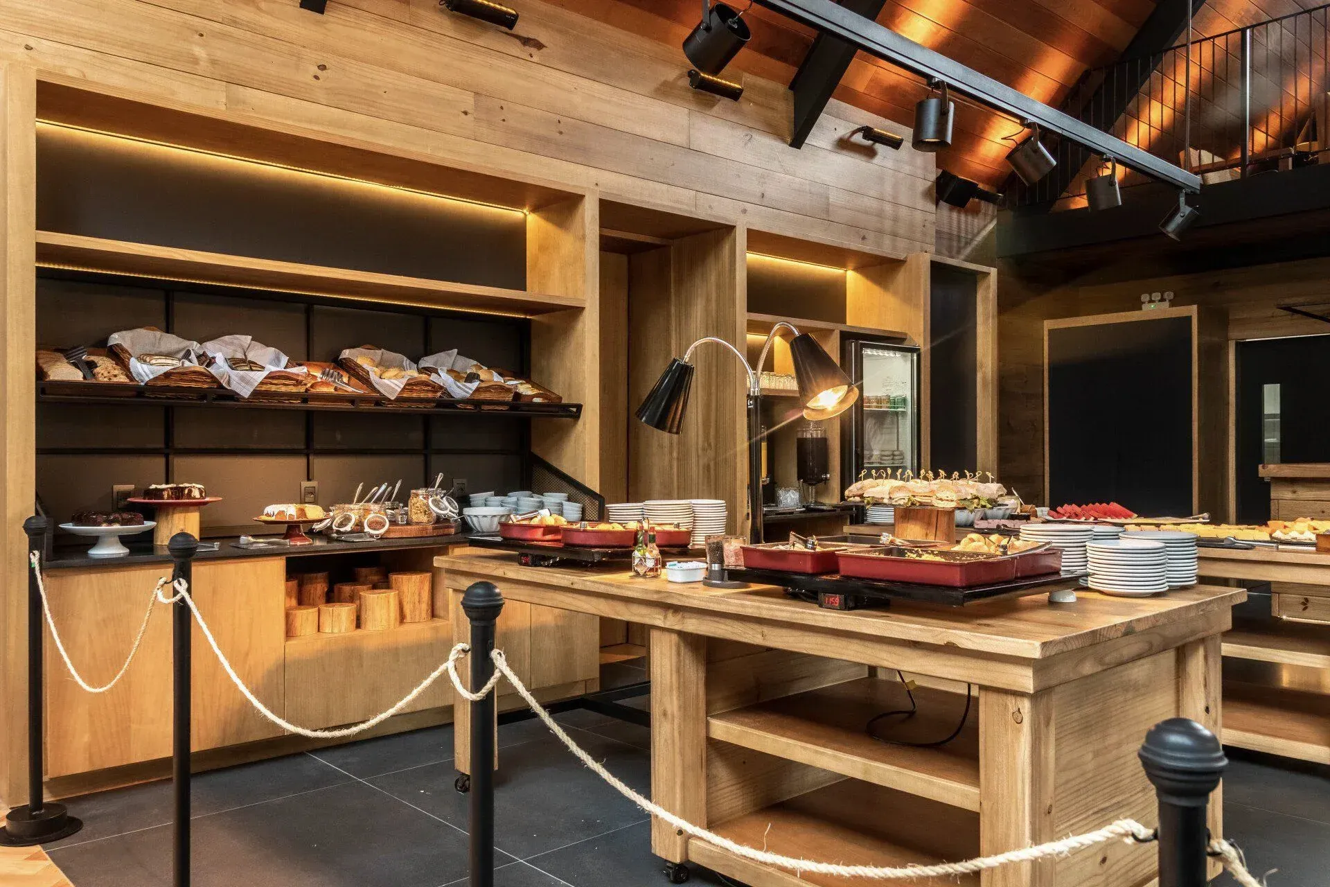 Balcão de buffet de madeira com doces e pratos em uma sala de jantar rústica e com iluminação aconchegante.
