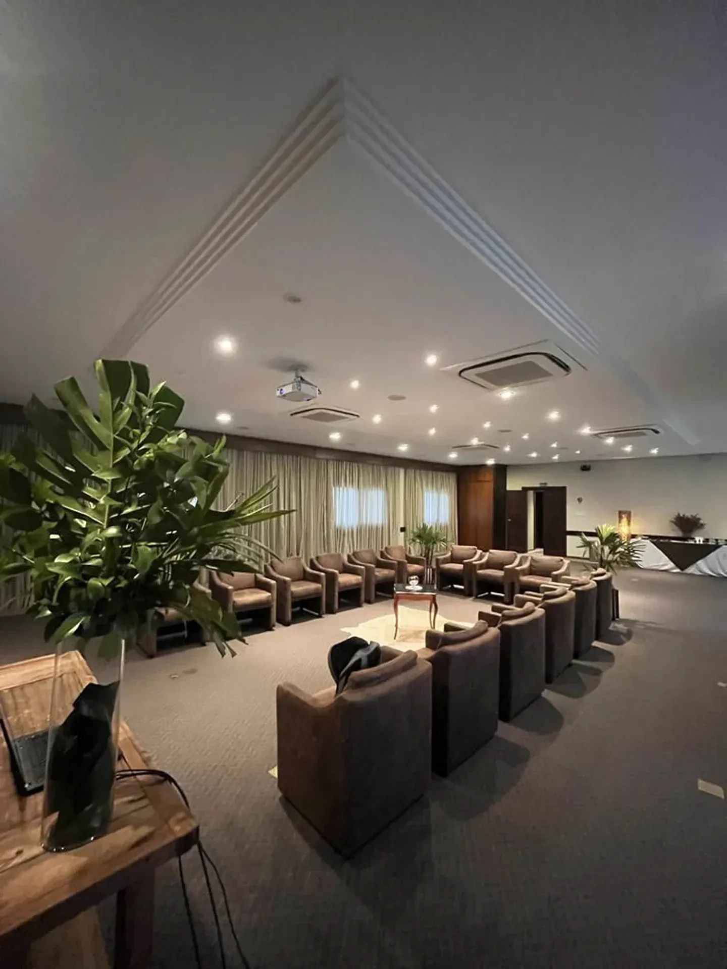 Sala de estar moderna com fileiras de cadeiras marrons, plantas em vasos, iluminação embutida e teto abobadado.