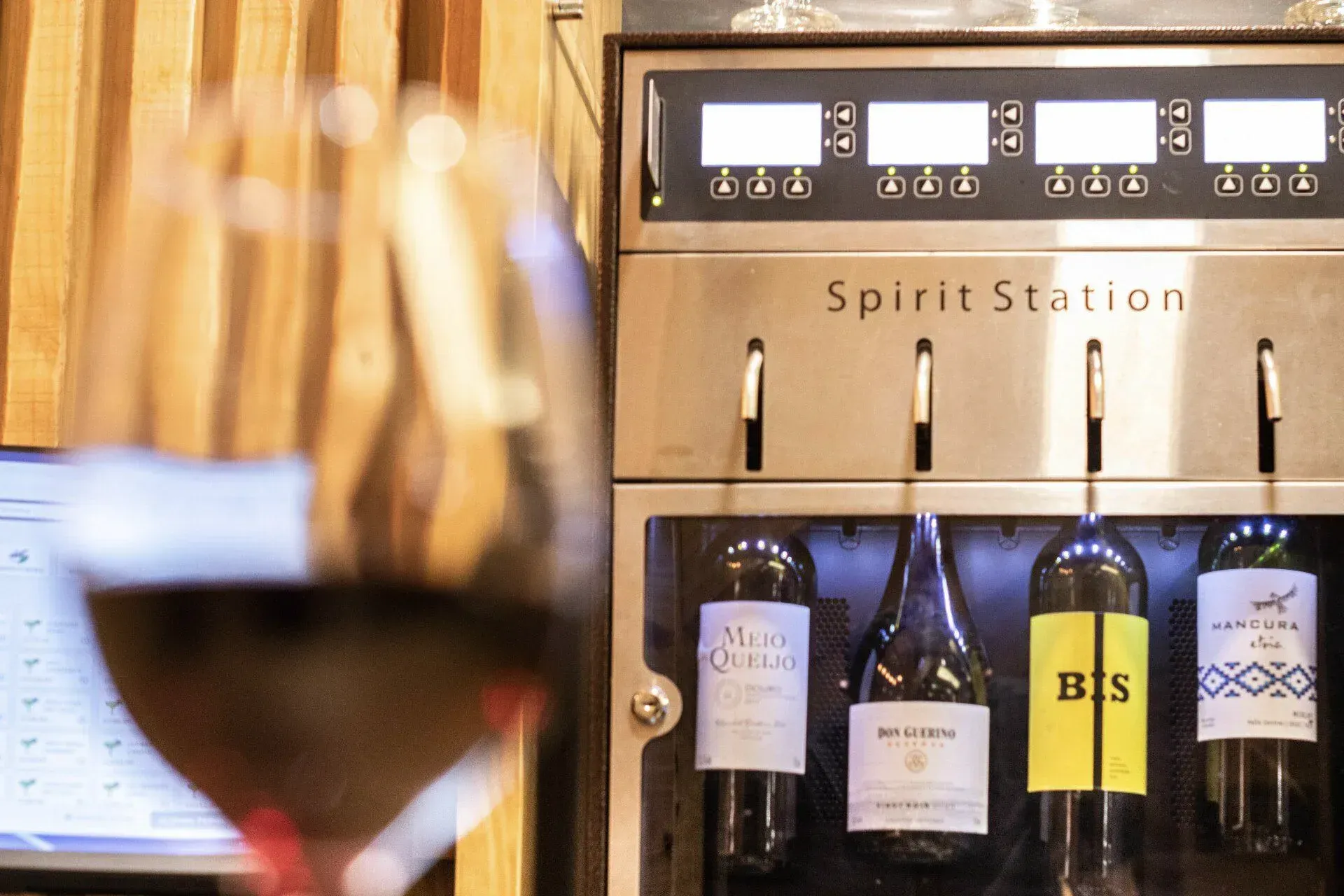 Taças de vinho em primeiro plano, com um dispensador de vinho Spirit Station e garrafas ao fundo.