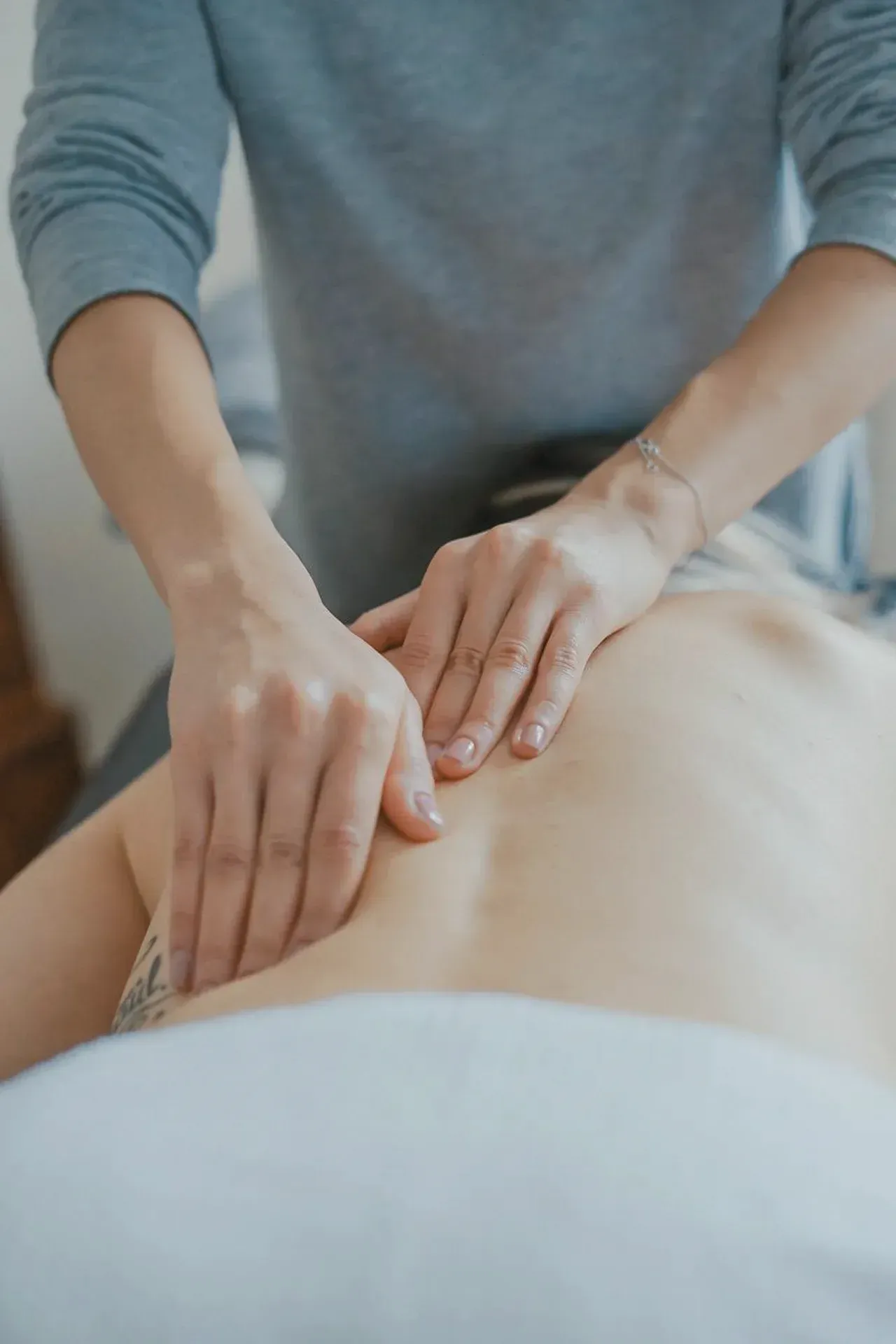 Mãos realizando uma massagem nas costas de uma pessoa deitada de bruços em uma cama.