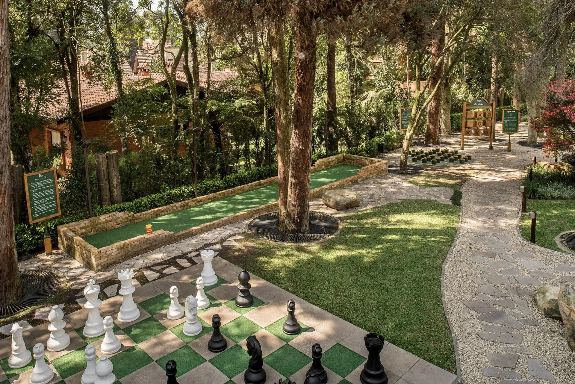 Jogo de xadrez ao ar livre com peças pretas e brancas de tamanho grande em um caminho de jardim ao lado de bancos e árvores.